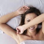 Portrett av en vakker dame som ligger i sengen og tenker på sine sexfantasier. Hun ser litt flau ut og gjemmer ansiktet sitt